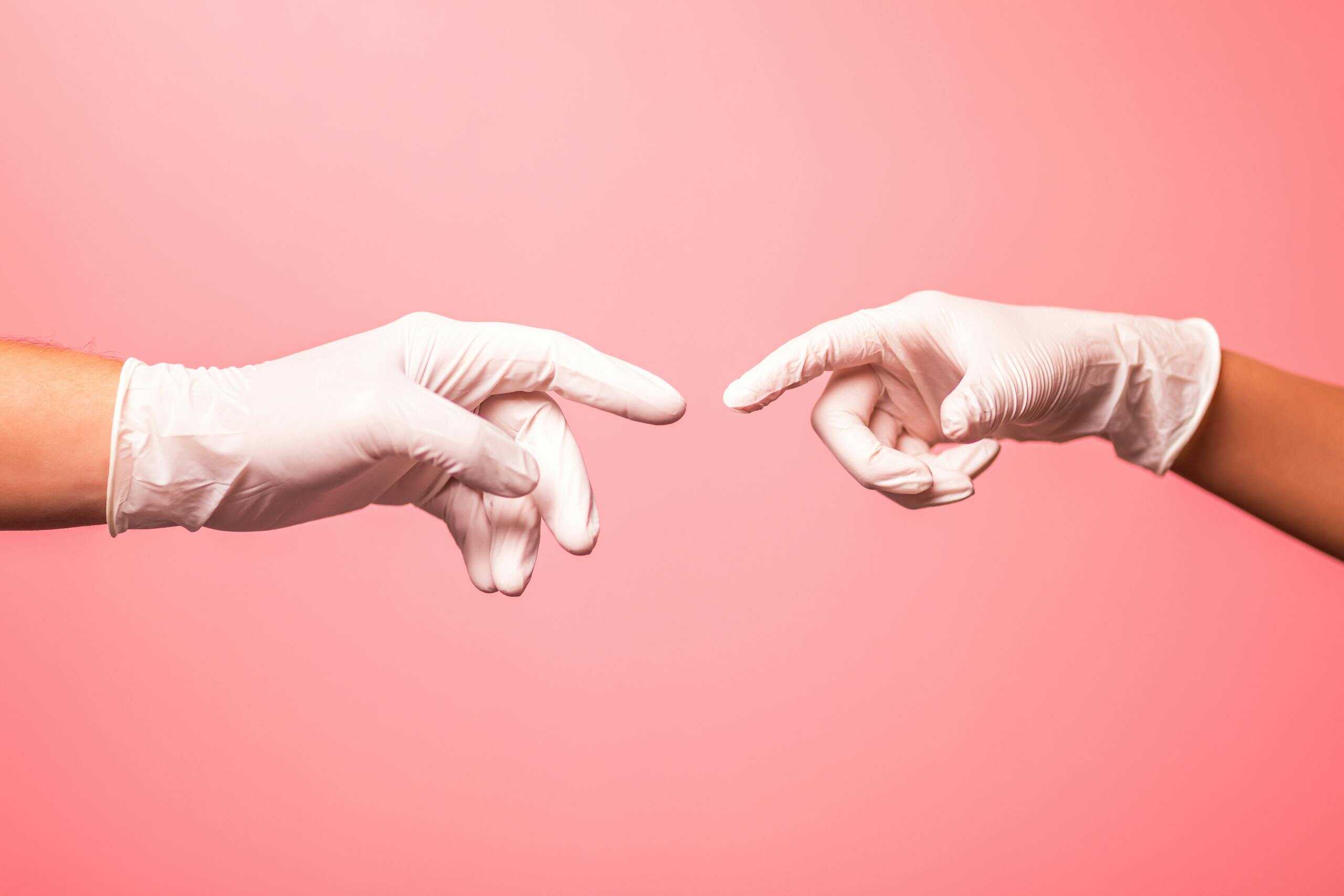 Close-up of hands in surgical gloves reaching out against a pink background.