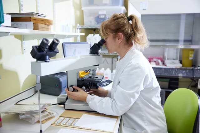a woman in a lab looking into a microscope